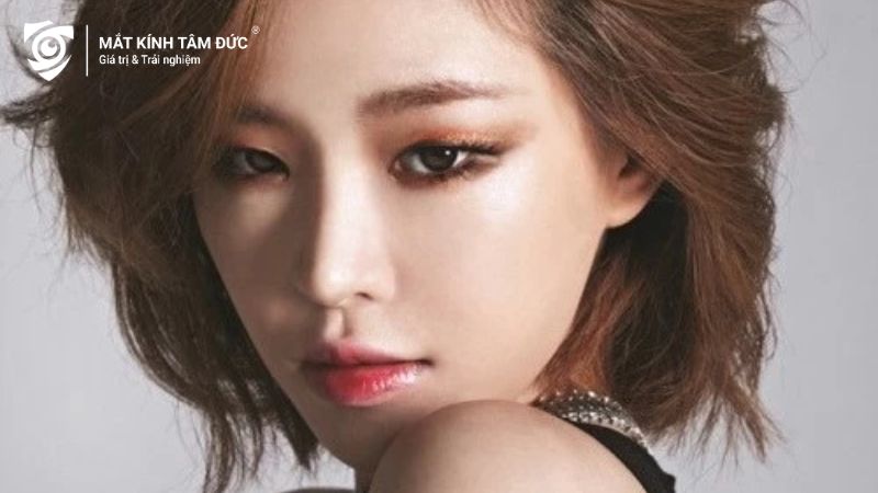 Hình ảnh của một người phụ nữ với mắt xếch, nhìn sang một bên với vẻ quyến rũ và tự tin. Cô ấy có mái tóc ngắn, xoăn nhẹ, cùng vẻ ngoài thanh thoát và sắc sảo.