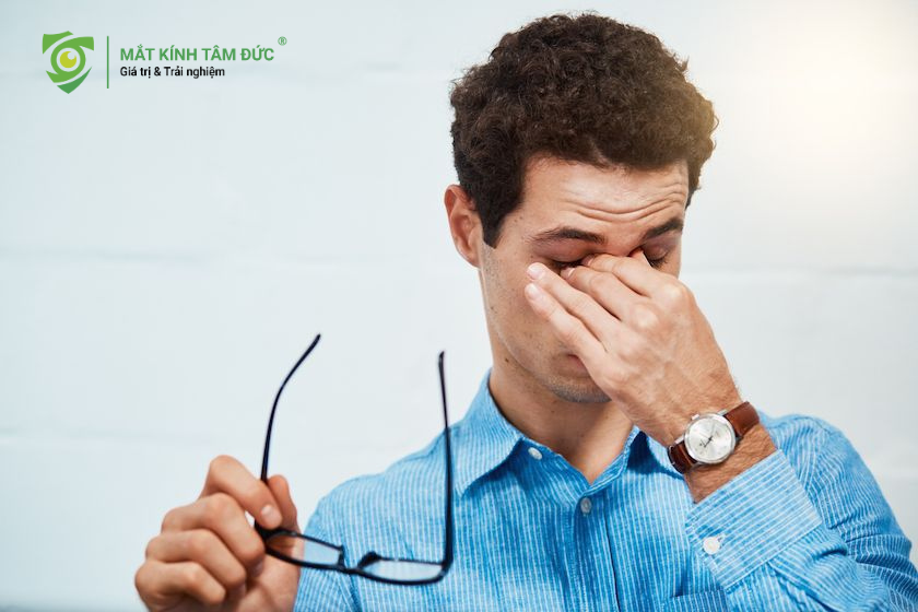 Người đàn ông mệt mỏi tháo kính và dụi mắt vì khó chịu hoặc căng thẳng thị giác khi ra đường