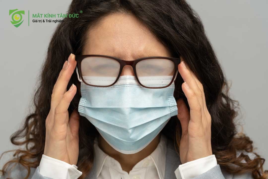 Hình ảnh một phụ nữ đeo khẩu trang, khó chịu do tròng kính bị mờ hoàn toàn bởi hơi thở hoặc hơi nước.
